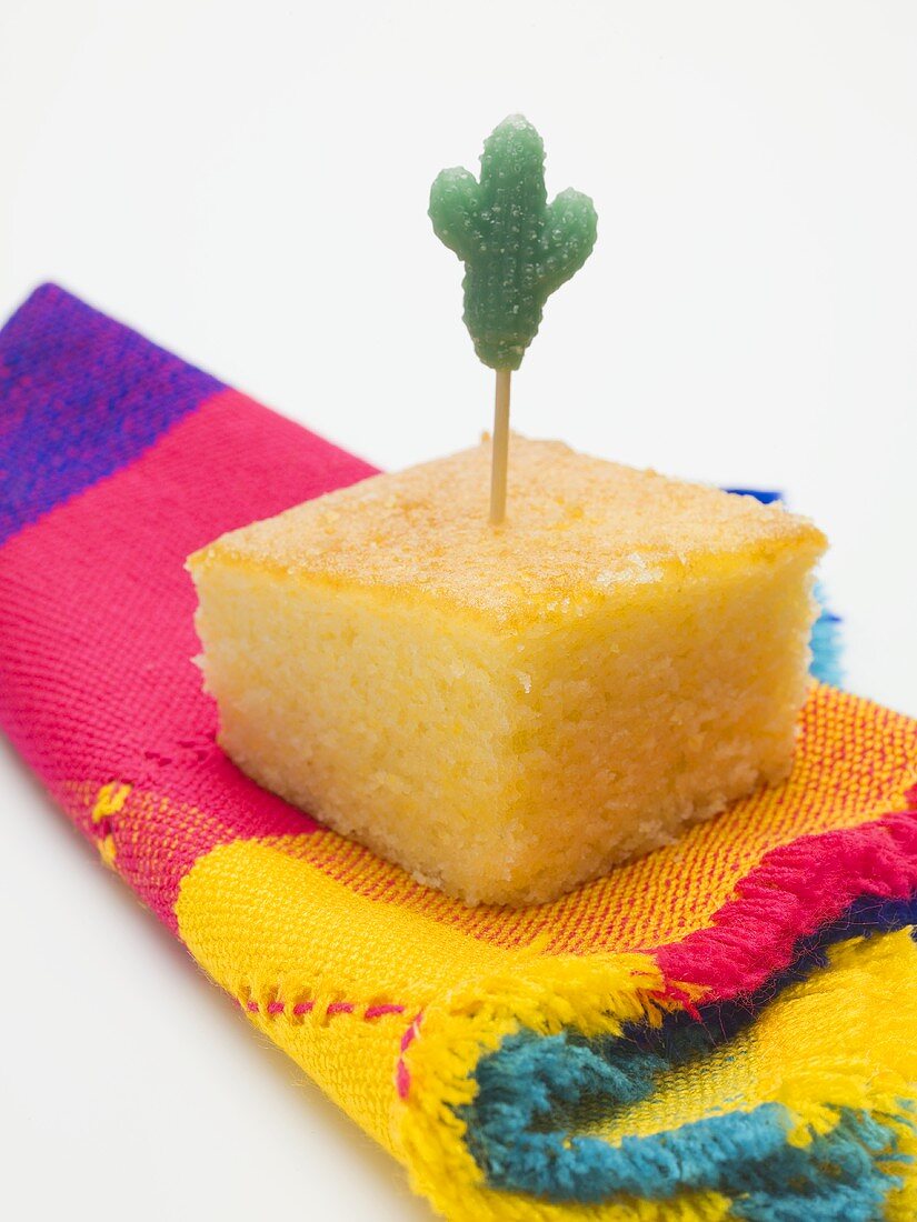 Cube of cornbread with cactus cocktail stick on cloth (Mexico)