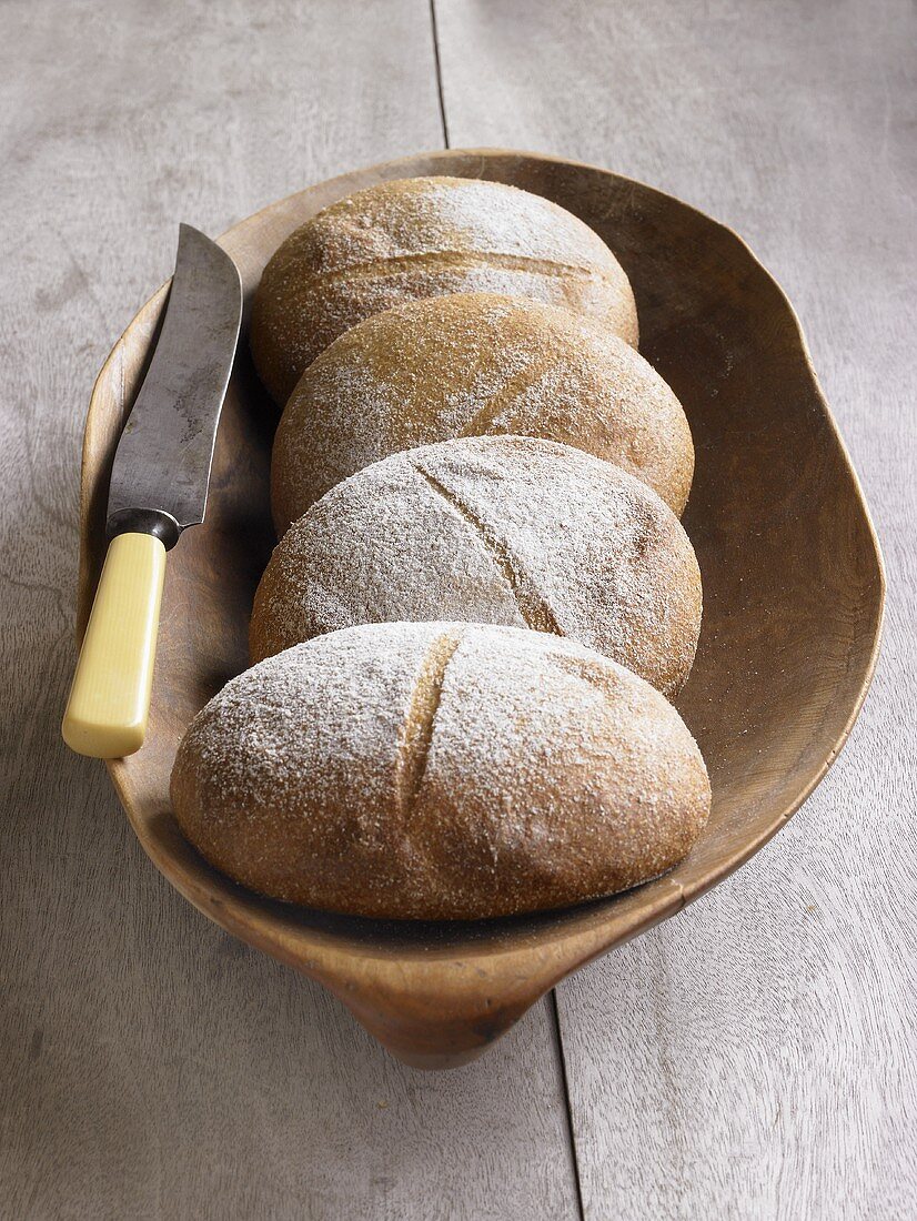 Four loaves of organic bread in wooden bowl with knife