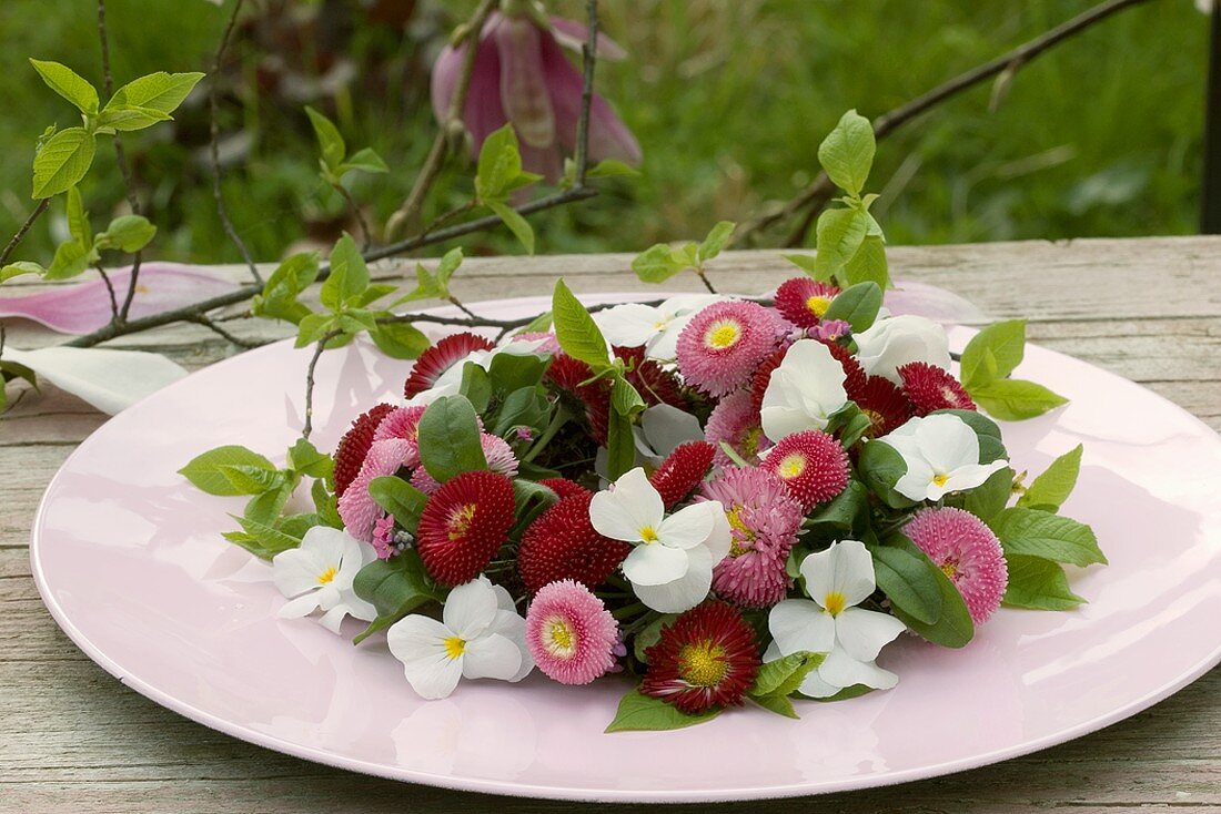 Kränzchen aus Bellis und Hornveilchen auf Tisch im Freien