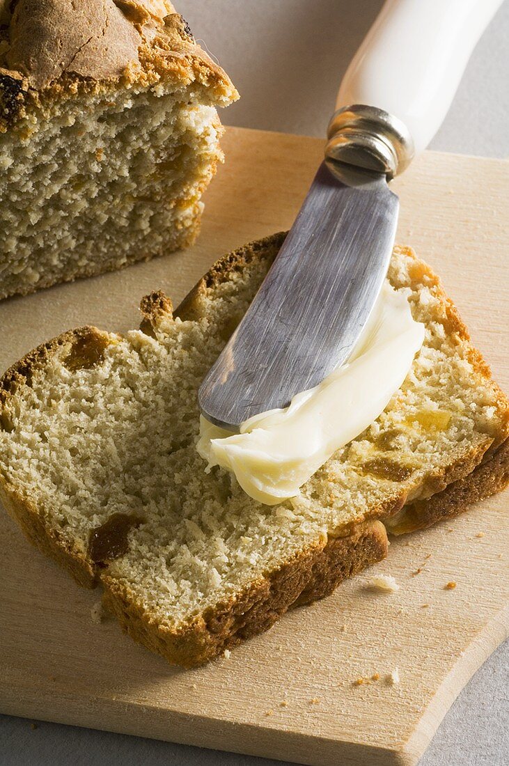 Buttering a slice of chestnut and apricot bread