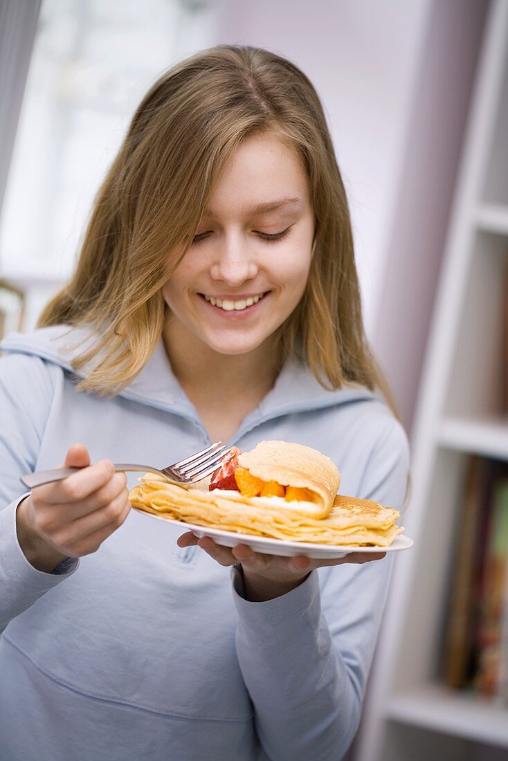 Mädchen isst Pfannkuchen mit Früchten und Sahne