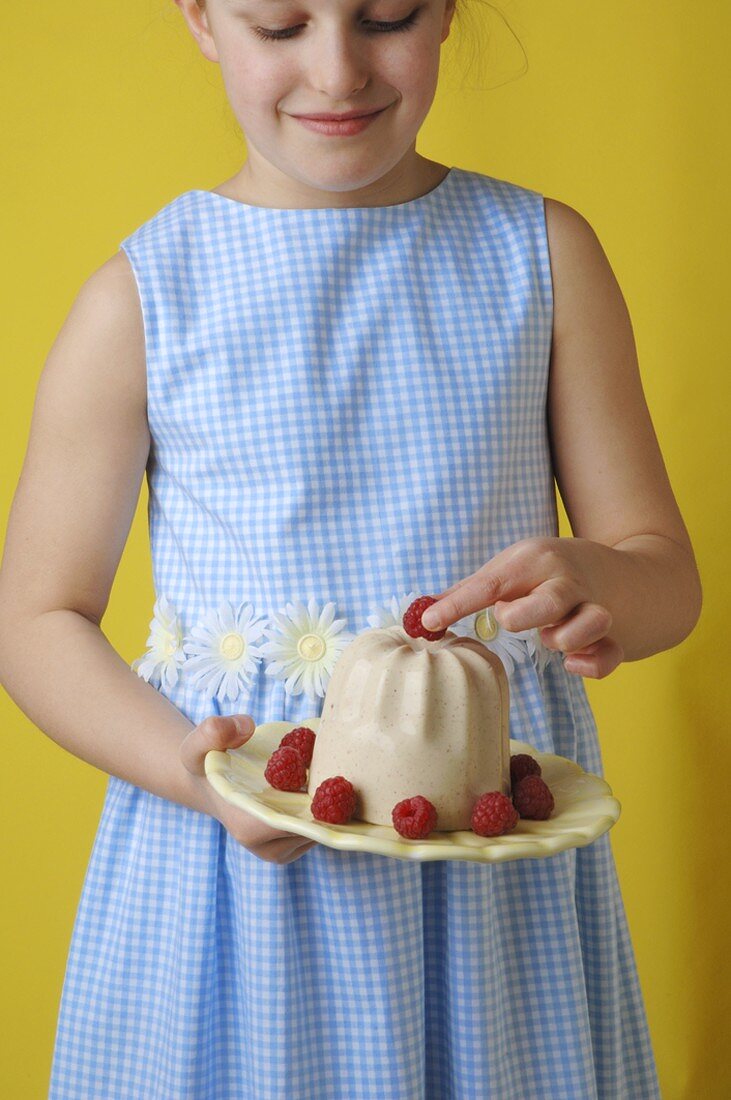Girl holding vanilla blancmange with raspberries