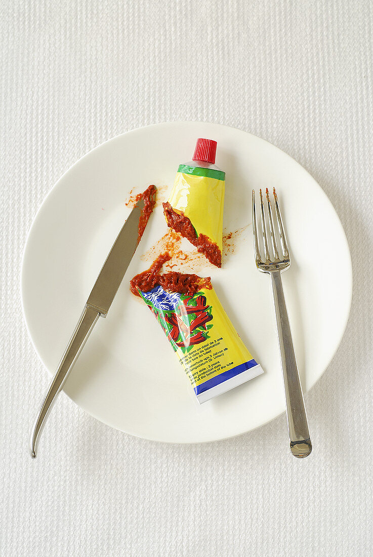 Tube of chilli puree, cut in half, on plate with cutlery