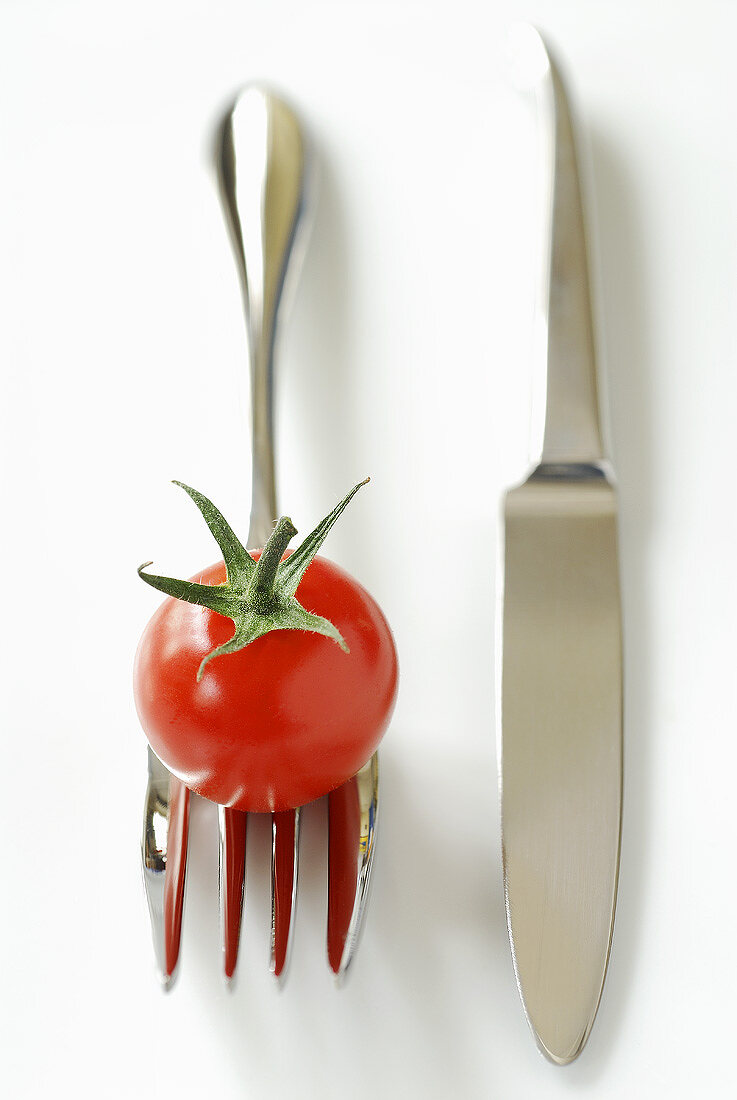 Cherry tomato on fork beside knife