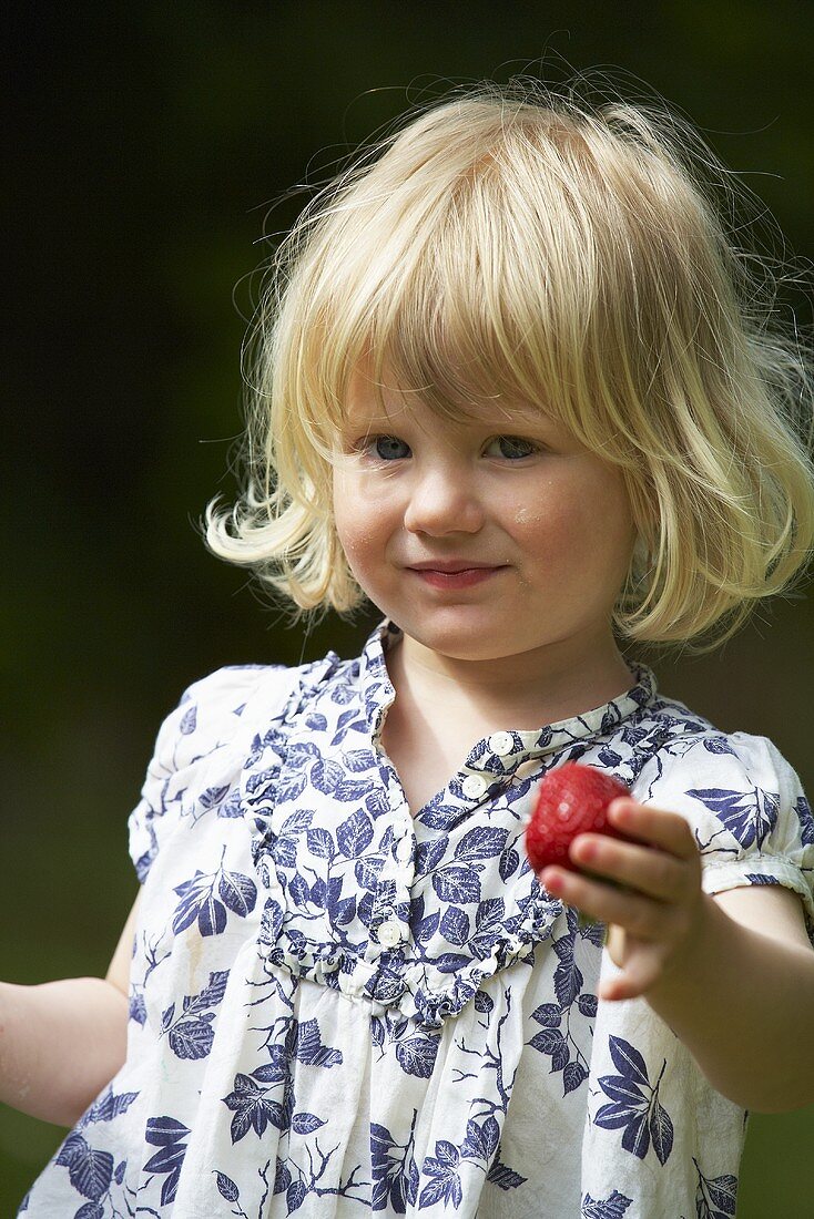 A little blonde girl holding a strawberry