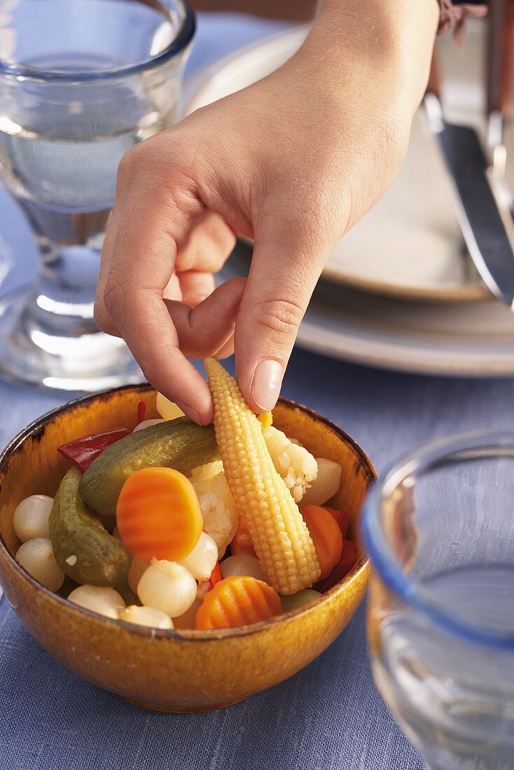 A hand taking a small, pickled corn cob