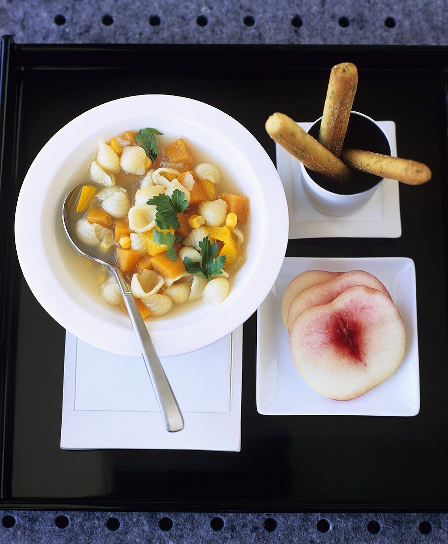 Noodle soup with vegetables, bread sticks and peach slices