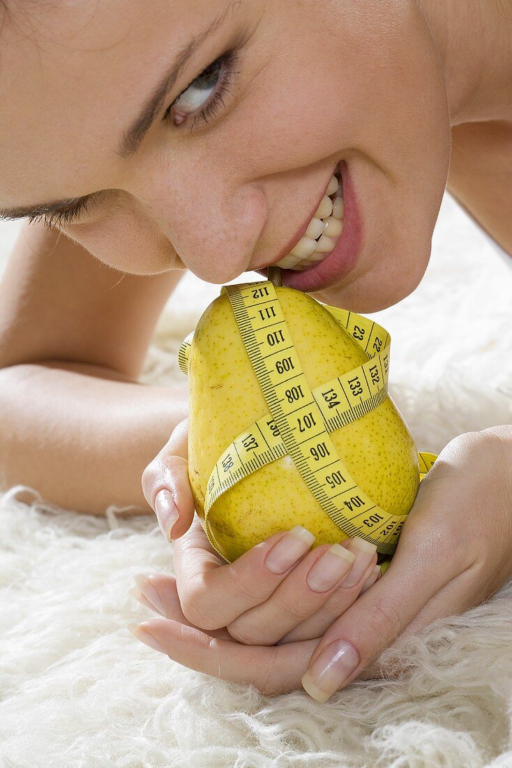 Young woman holding pear with tape measure