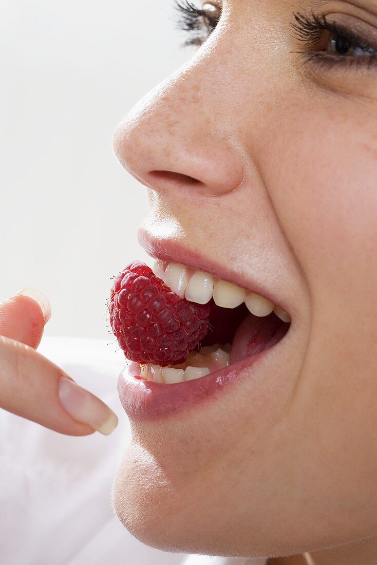 Young woman holding a raspberry in her mouth