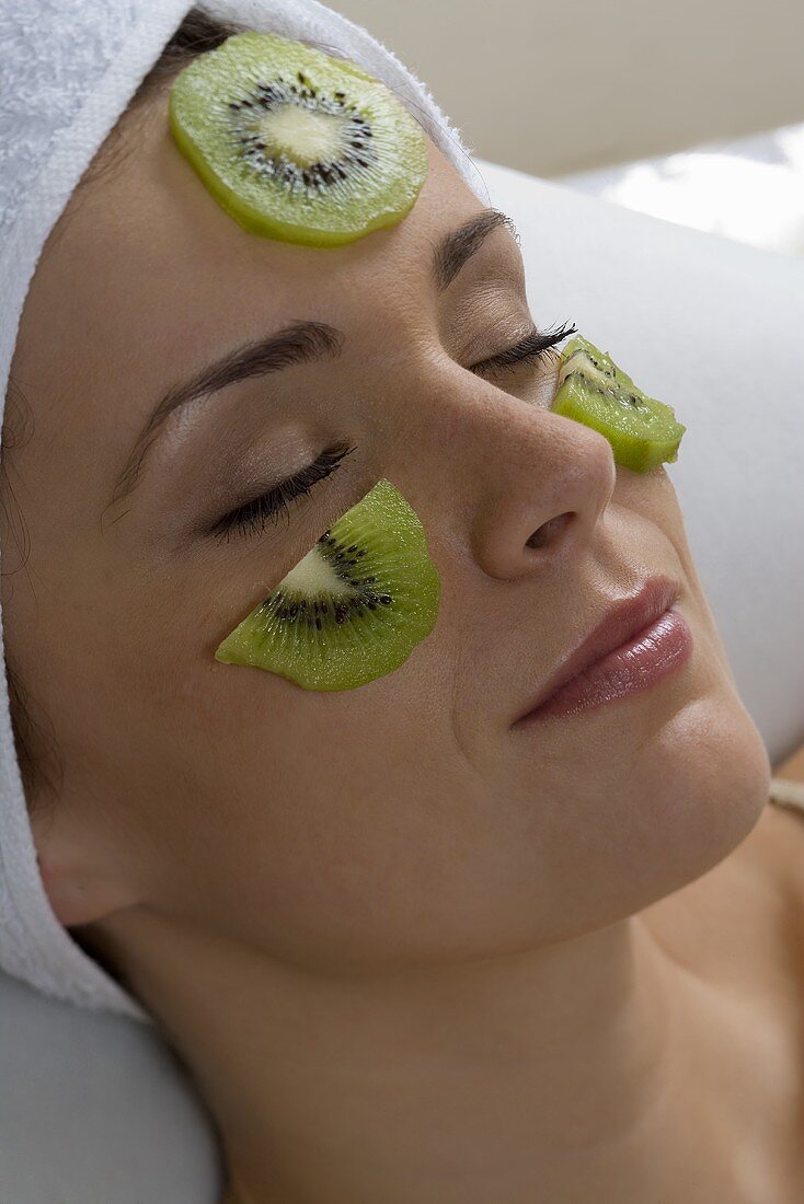 Young woman with slices of kiwi fruit on her face