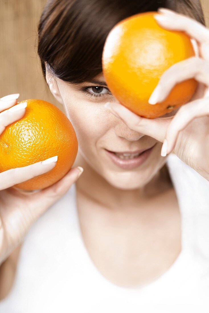 Junge Frau hält zwei Orangen vor ihr Gesicht
