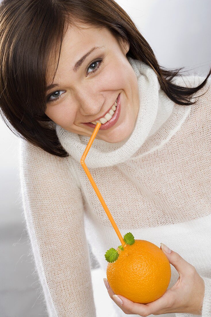 Junge Frau trinkt Saft aus Orange mit Strohhalm