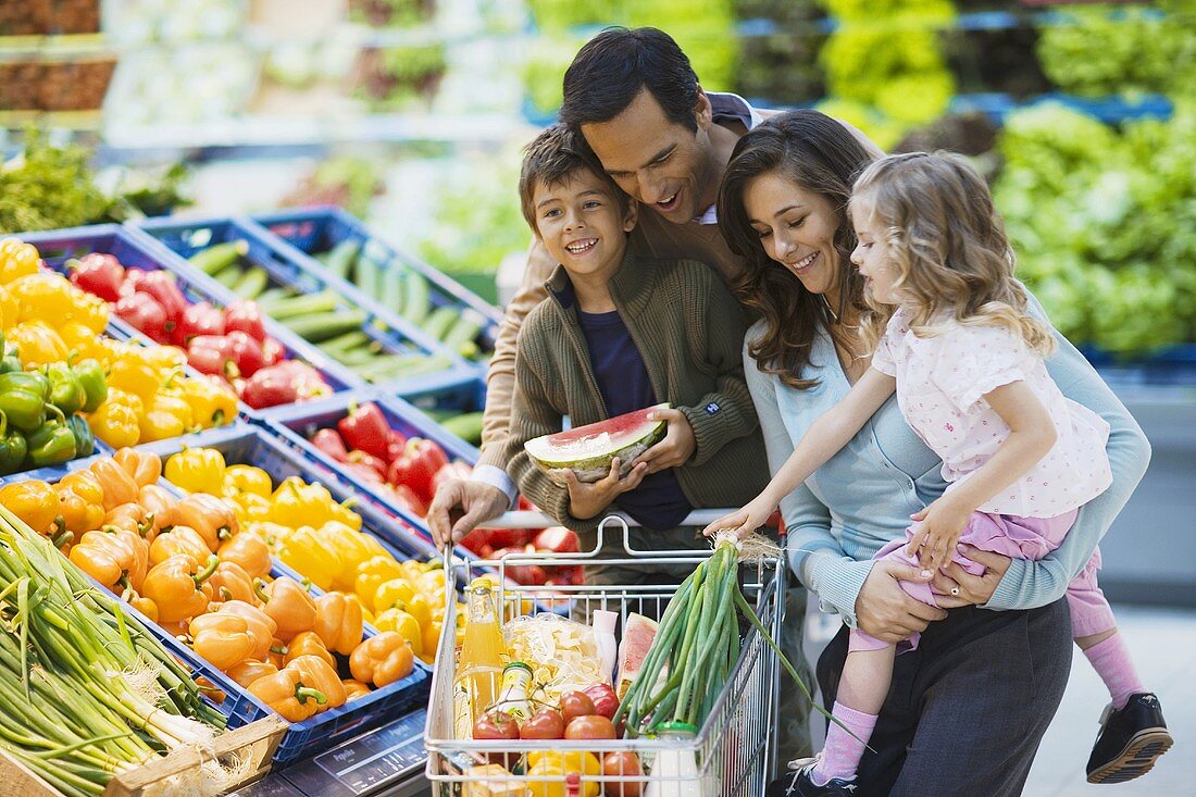 Familie mit vollem Einkaufswagen am Gemüsestand im Supermarkt