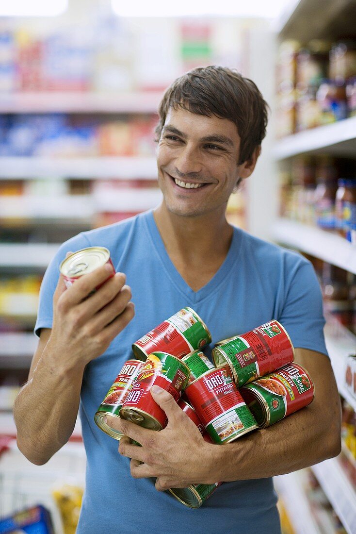 Junger Mann kauft Dosentomaten in einem Supermarkt ein