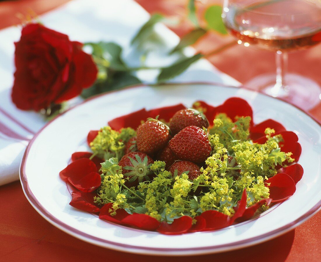 Teller mit frischen Erdbeeren, Rosenblüten und Frauenmantel