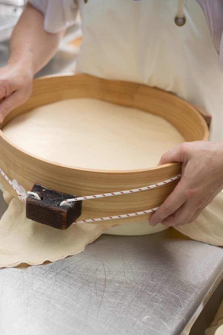 Cheese dairy worker holding round cheese in wooden mould