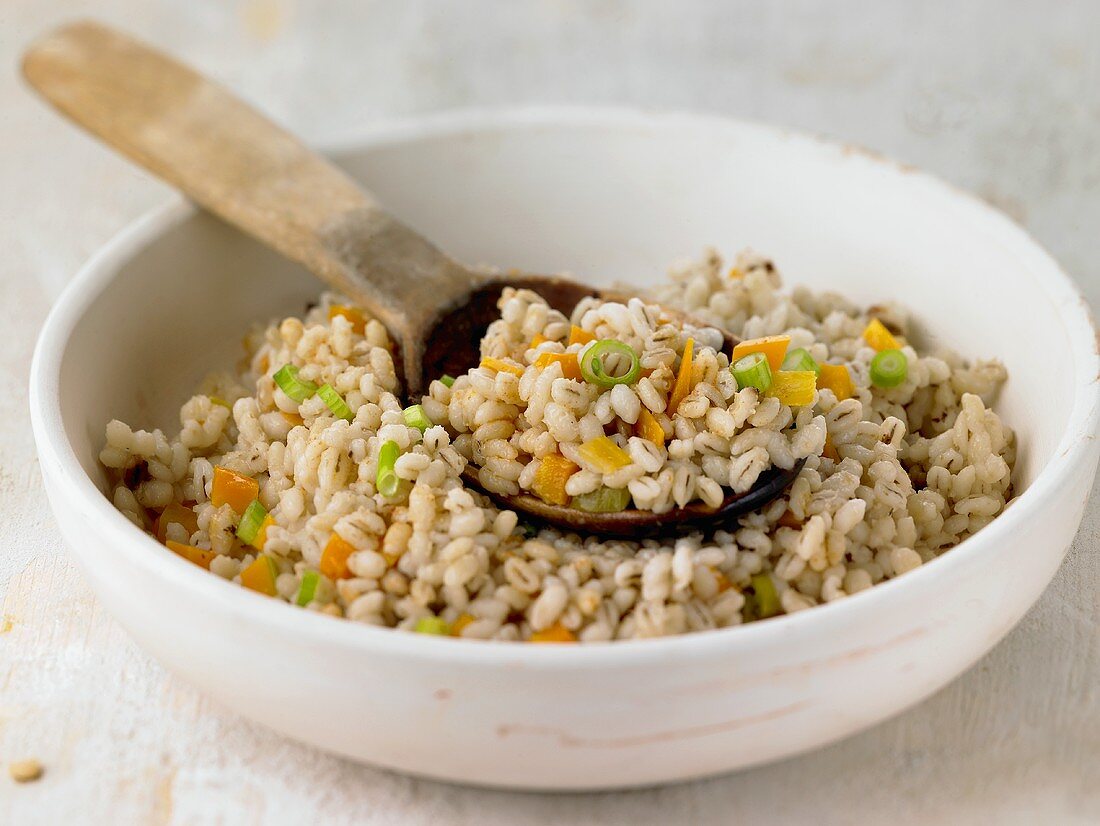 Pearl barley with vegetables in bowl with wooden spoon