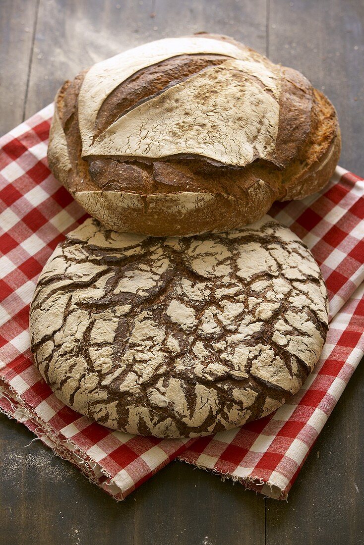 Zwei rustikale Brotlaibe auf kariertem Tuch