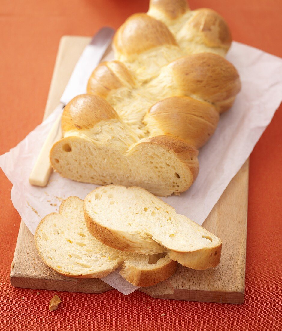 Bread plait, partly sliced, on chopping board