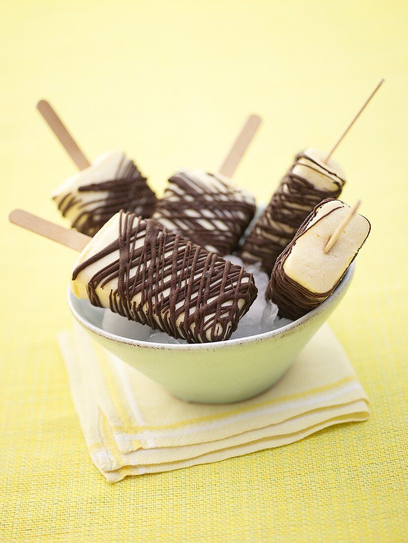 Chocolate-coated banana ice cream lollies in bowl of ice cubes