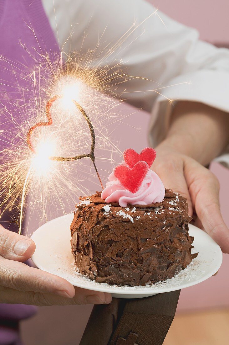 Woman holding small chocolate cake with sparkler