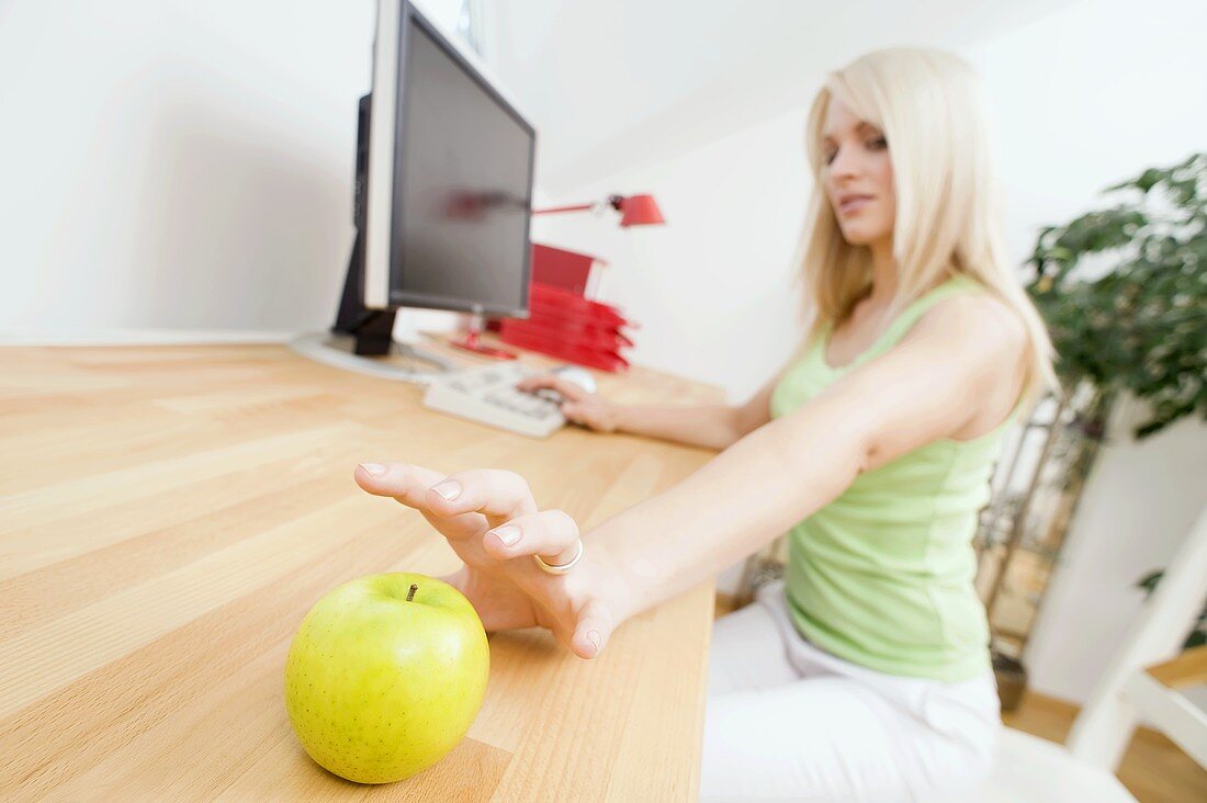 Frau greift nach Apfel auf Bürotisch