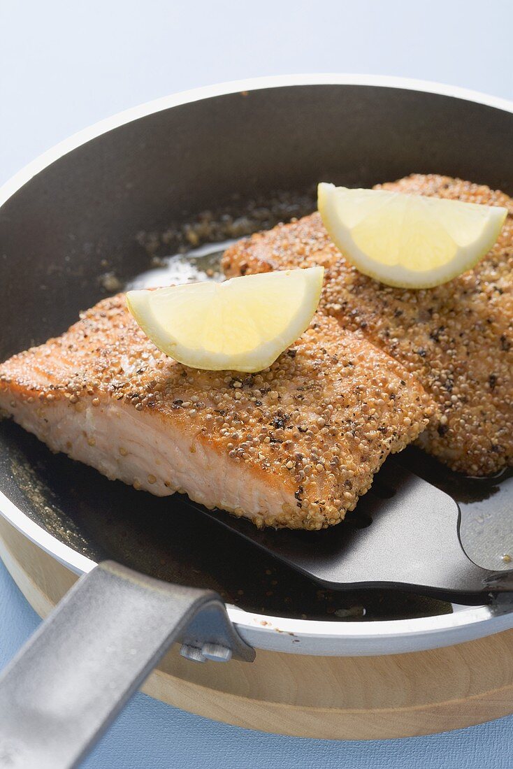 Fried salmon fillet with lemon wedges in frying pan