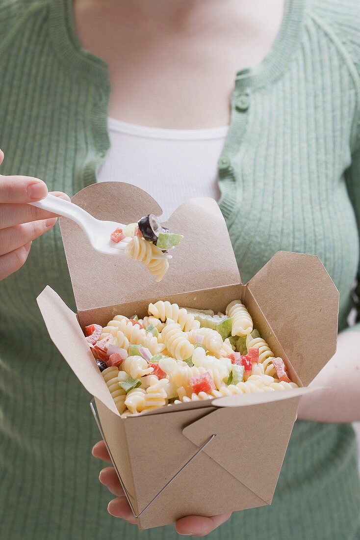 Woman eating pasta and vegetables out of take-away box