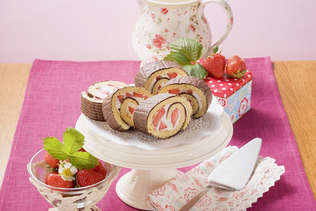 Biskuitrolle mit Erdbeeren und Schokoglasur auf Tortenständer