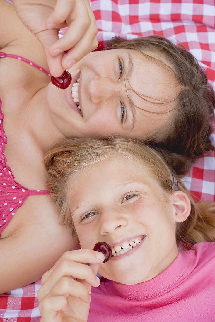 Zwei Mädchen mit Kirschen auf Picknickdecke