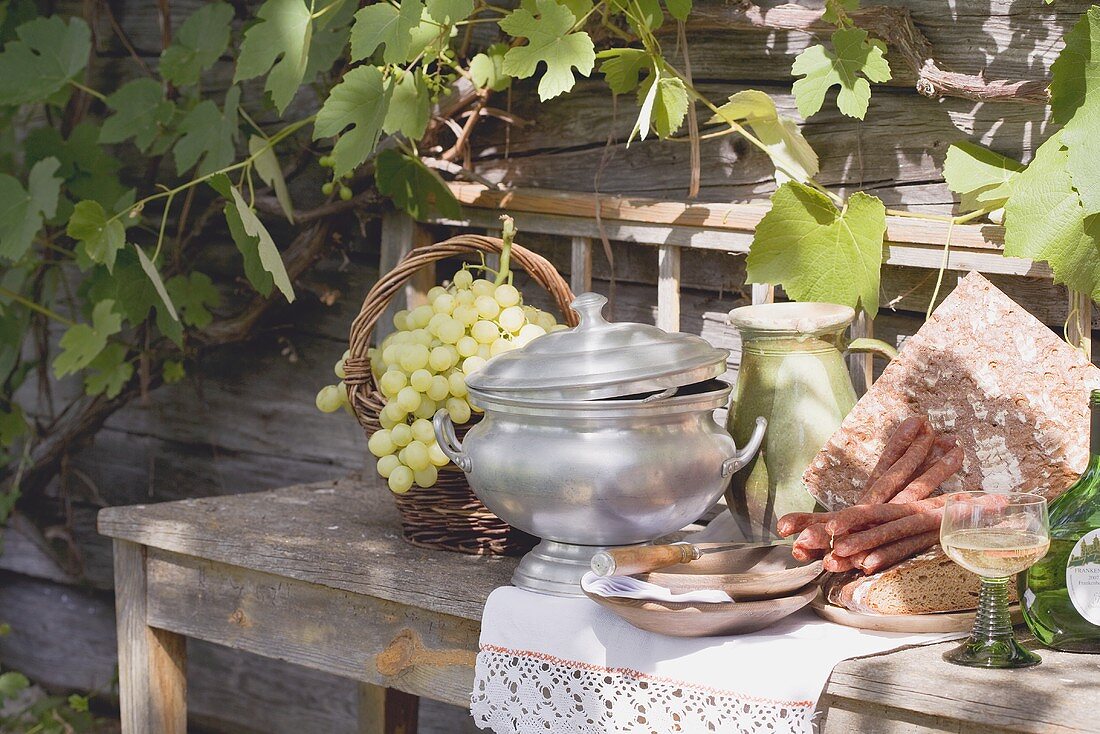 Stillleben mit Trauben, Brot, Wurst und Wein vor Bauernhaus