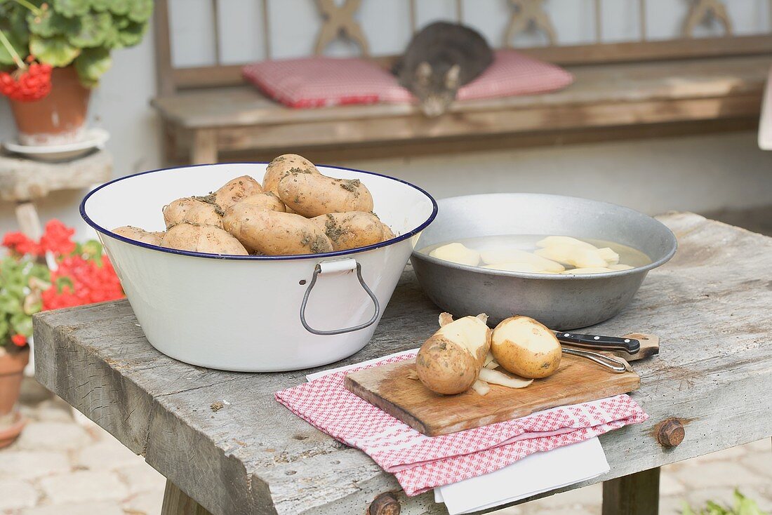 Potatoes, partly peeled, on table in front of farmhouse