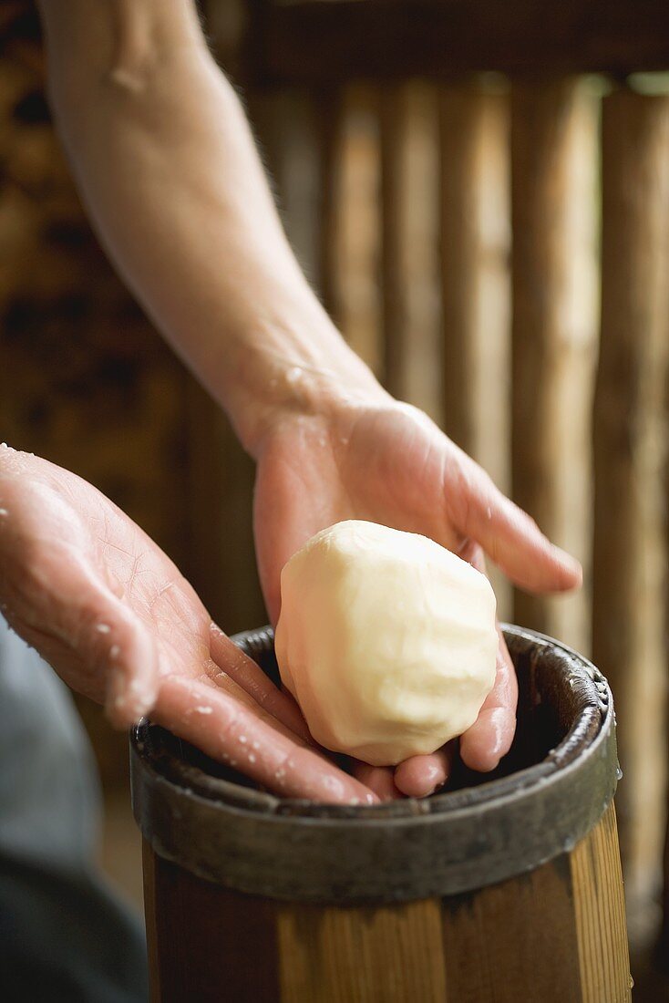 Hands holding a ball of butter over a butter churn
