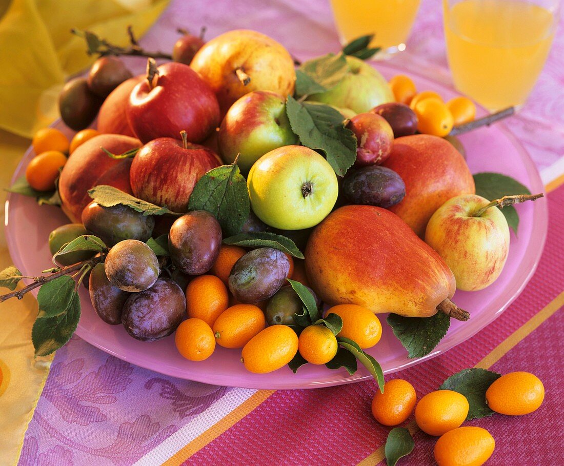 Apples, pears, plums and kumquats on plate