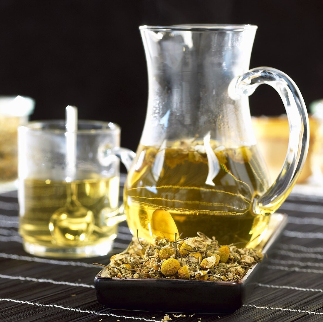 Chamomile tea in glass jug and glass cup, chamomile flowers