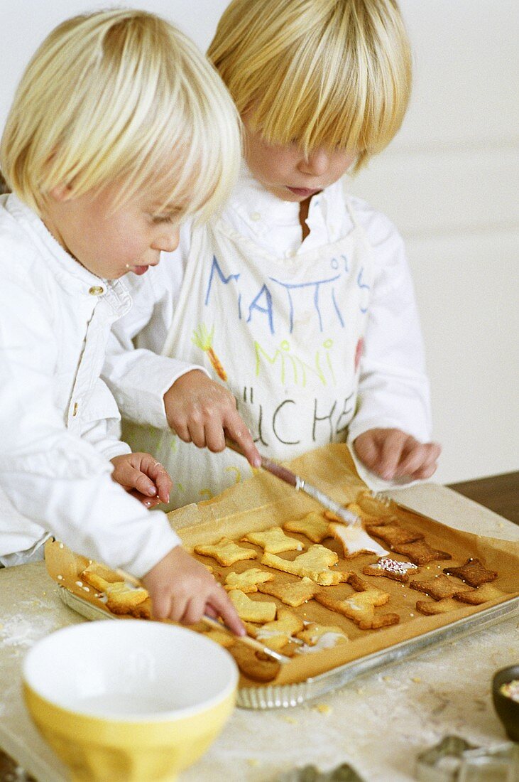 Zwei Kinder bestreichen Plätzchen mit Zuckerglasur