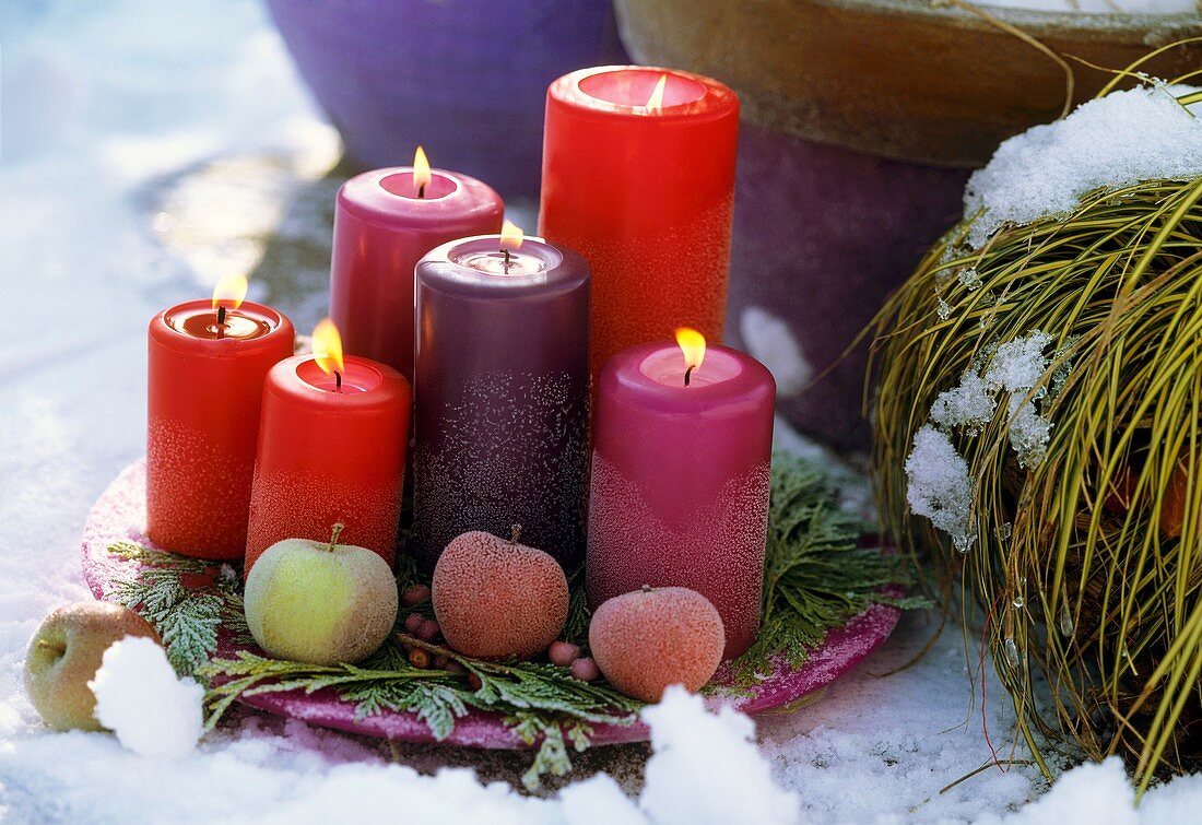 Plate with candles and ornamental apples in snow