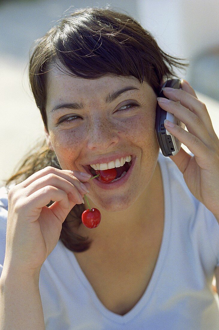 Young woman with a pair of cherries and a mobile phone