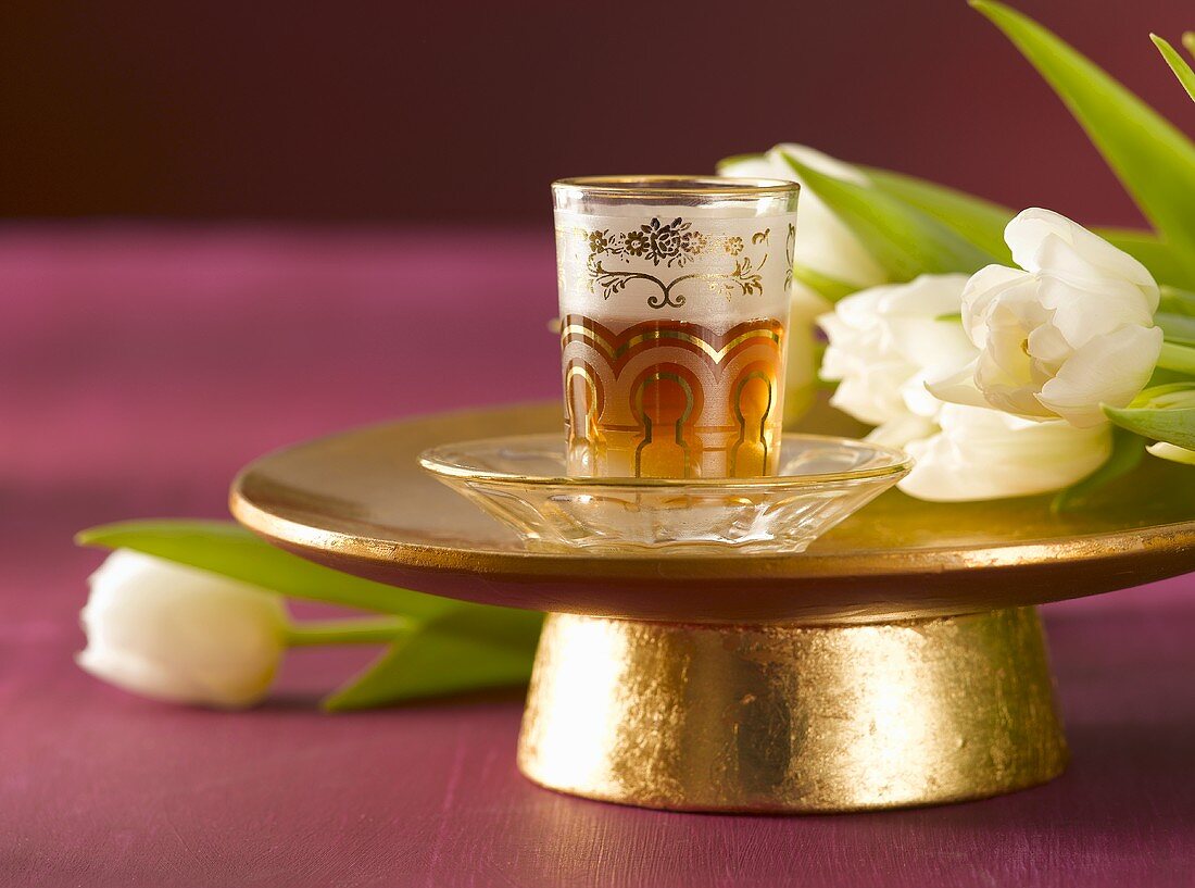 Tee im orientalischen Teeglas auf goldener Schale & Tulpen