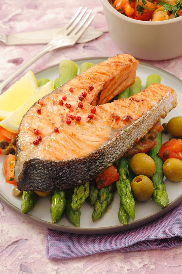 Salmon steak on green asparagus, olives and tomatoes