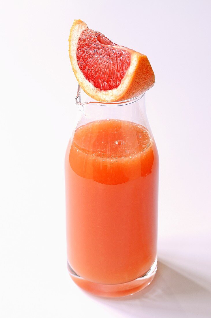 Wedge of pink grapefruit on carafe of grapefruit juice
