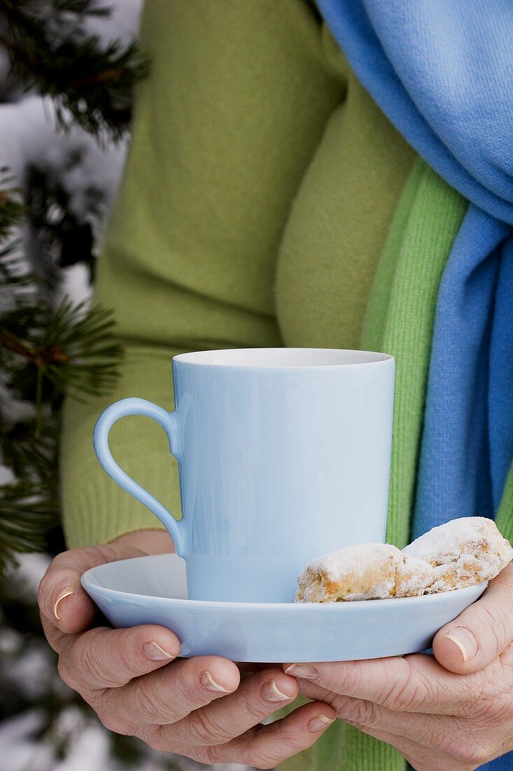 Hands holding a cup of hot chocolate and stollen cookies