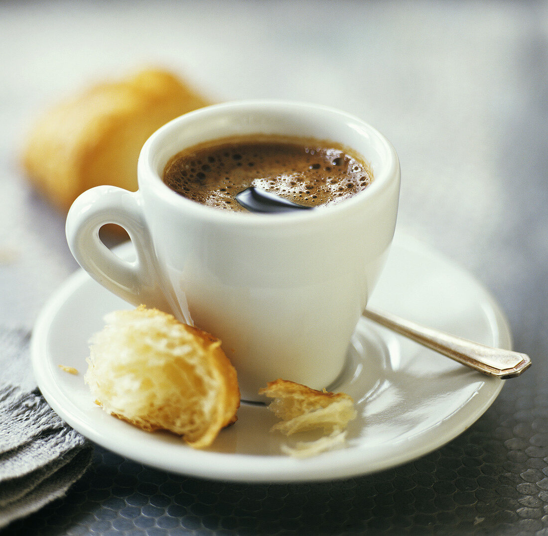 A cup of espresso with a croissant