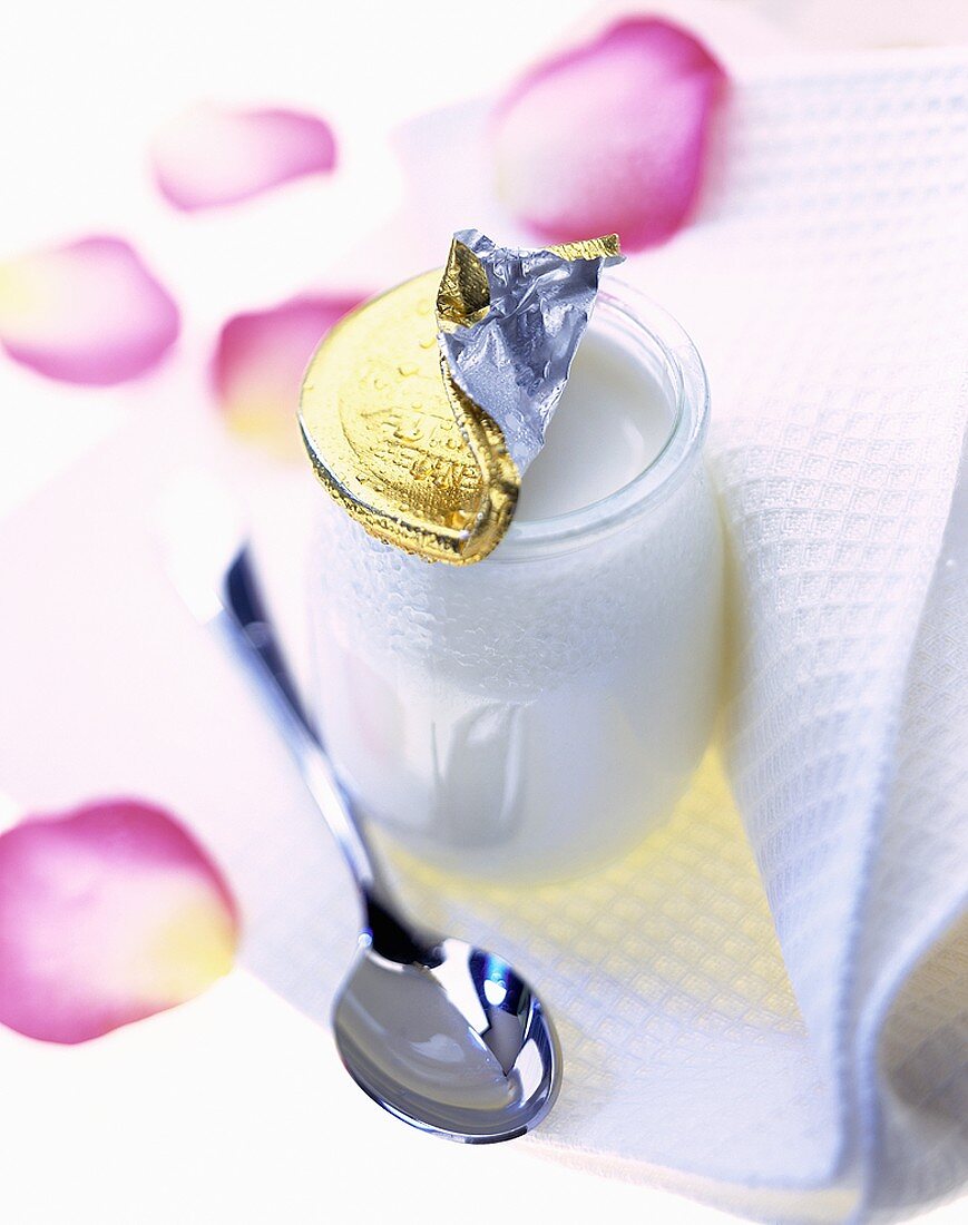 Jar of yoghurt with spoon on table mat with rose petals