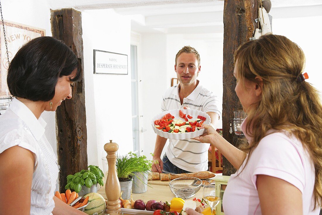 Young woman passing quiche dish with vegetables to young man