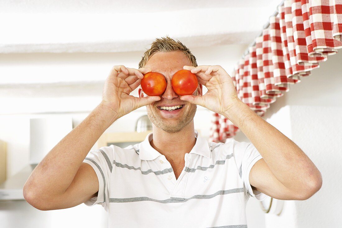 Junger Mann hält sich zwei Tomaten vor die Augen