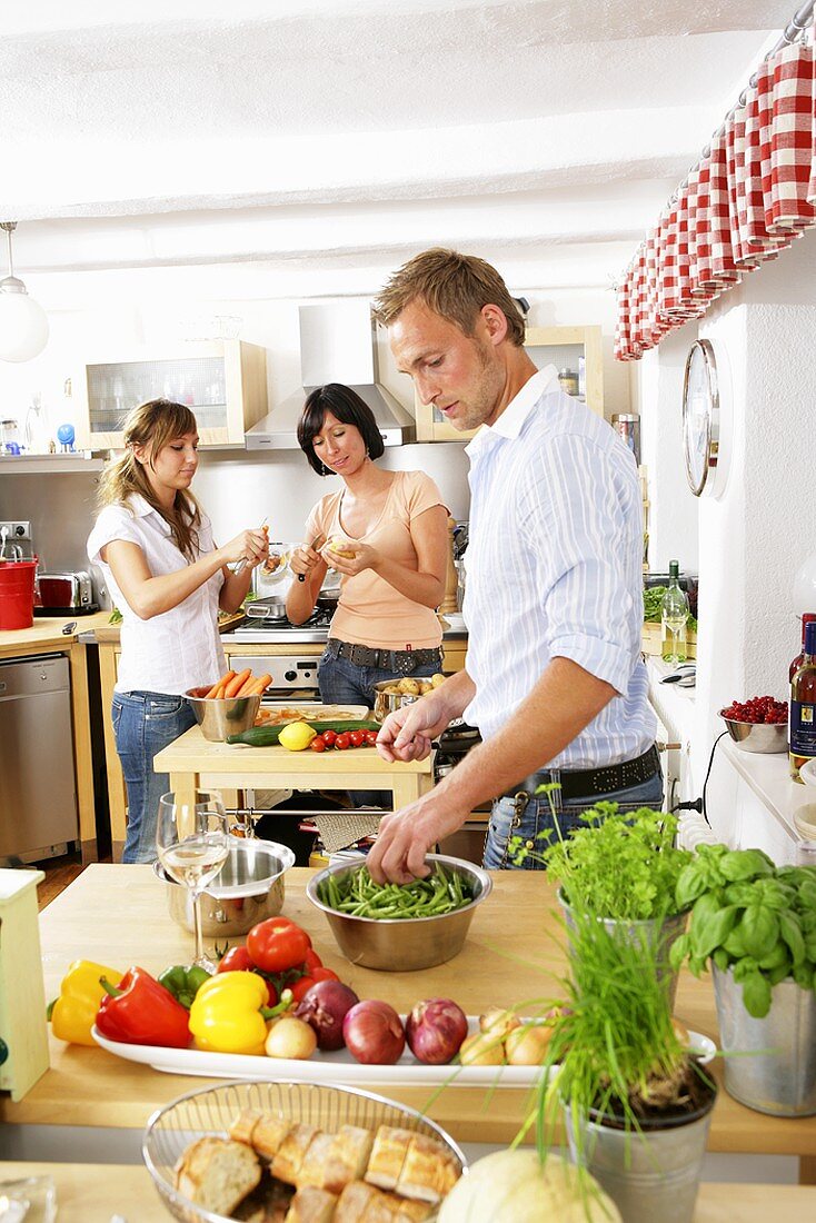 Drei junge Leute putzen Gemüse in der Küche