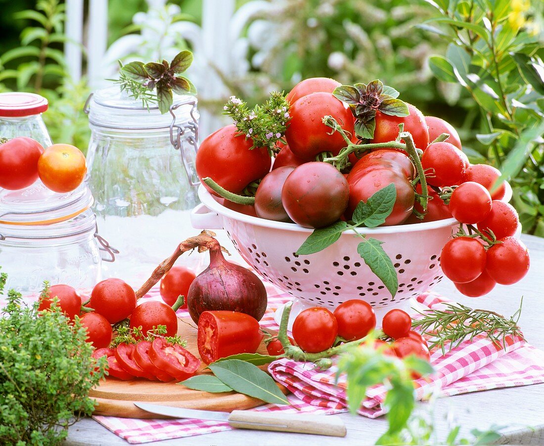 Tomatoes in colander & on chopping board, herbs & preserving jars