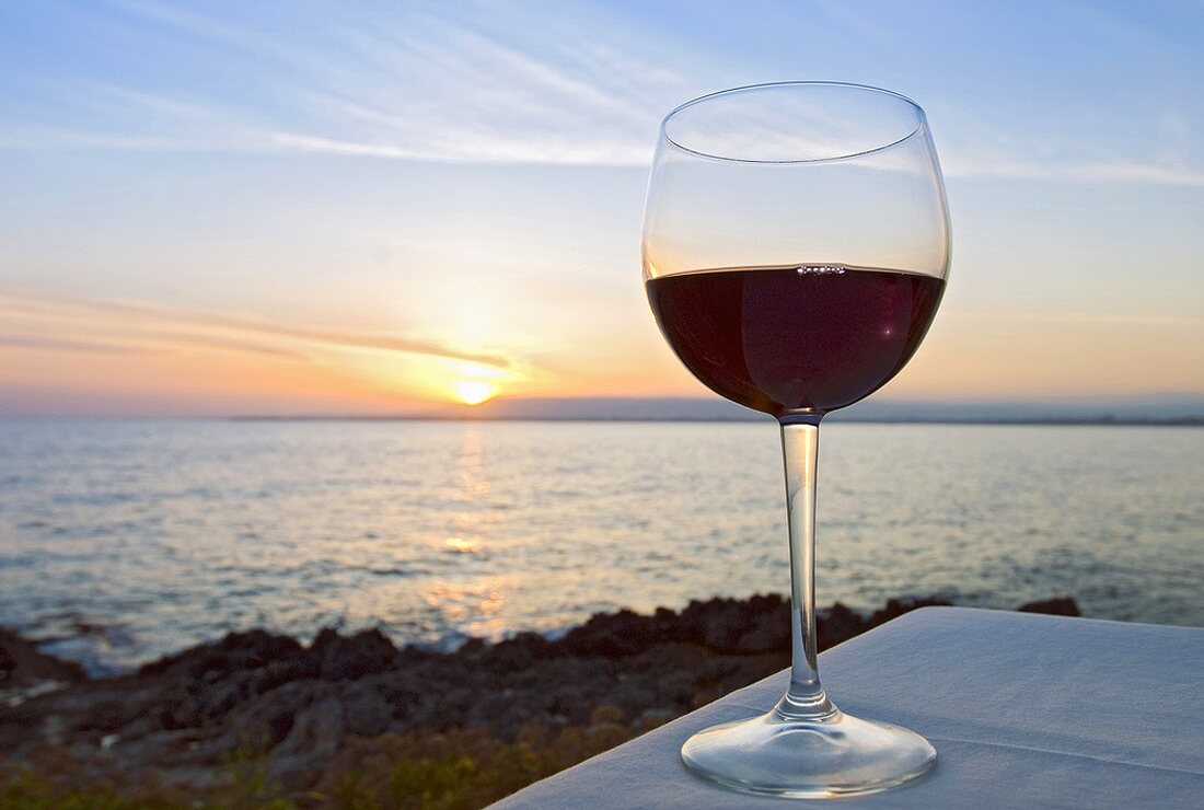 Ein Glas Rotwein vor Sonnenuntergang am See