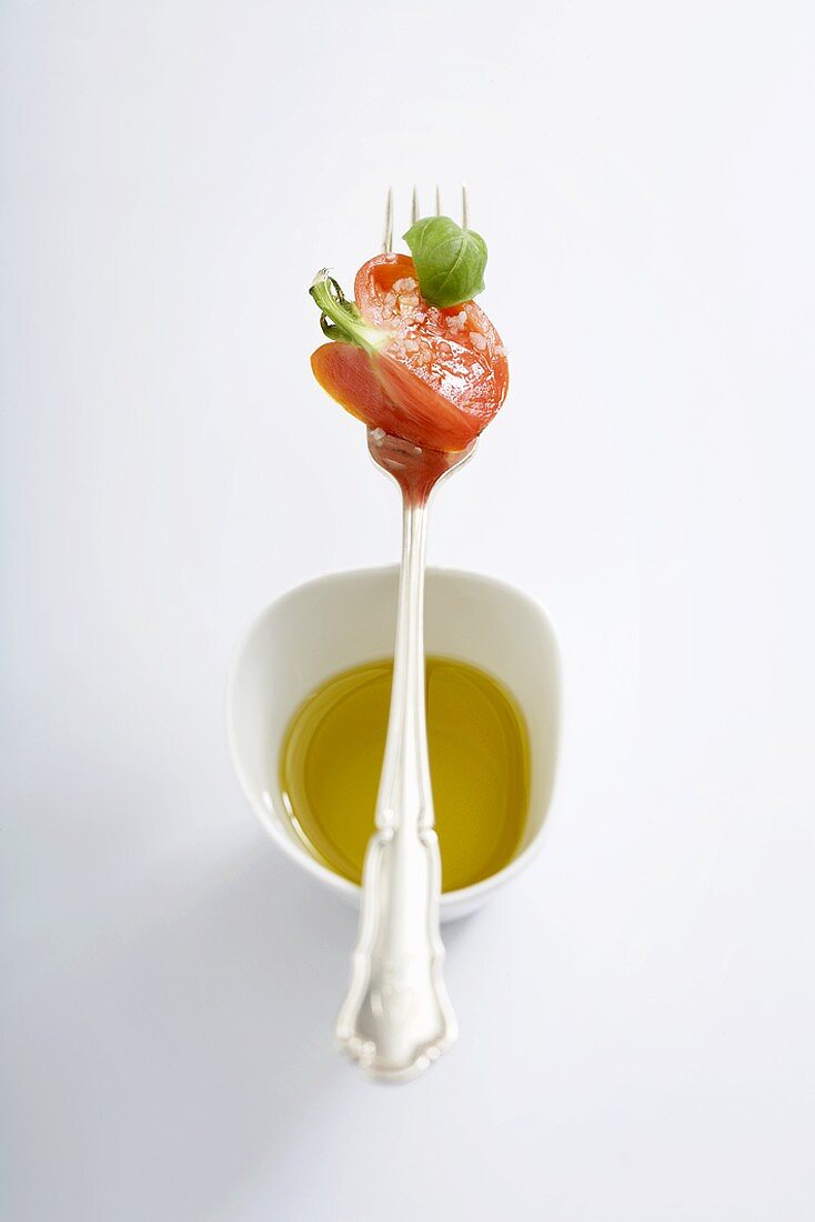 Tomato and basil on fork over small dish of olive oil